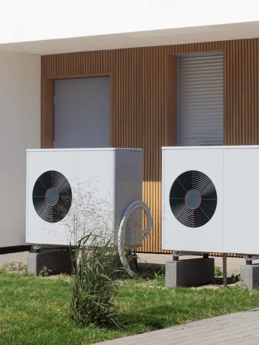 Two eco-friendly air source heat pumps situated in front of a modern house with a lush lawn, symbolizing green heating solutions.